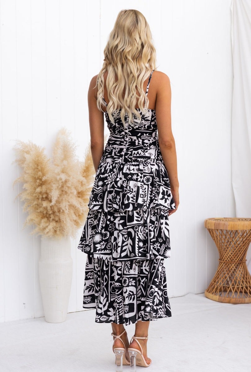 Back view of Rynn Midi Dress with adjustable straps, tie detail, and layered ruffle skirt in black print.