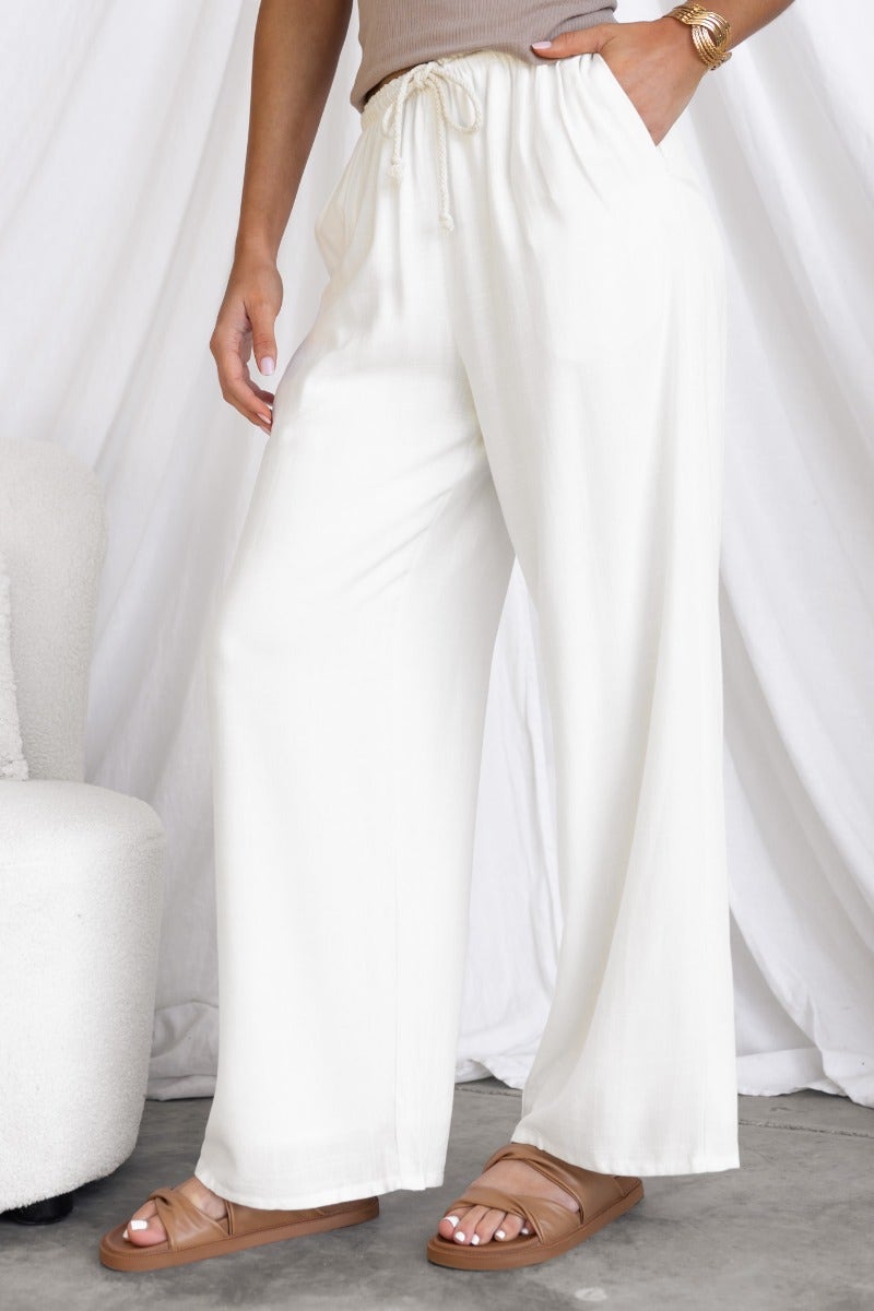 Model wearing white Corella Pants with a relaxed fit and drawstring waist, styled with casual sandals.