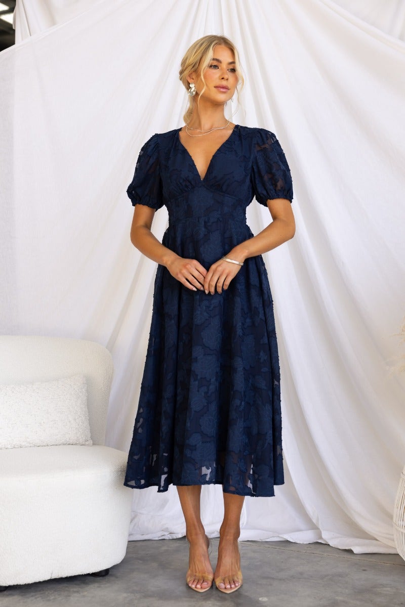Narella Midi Dress in navy, featuring embossed print, V-neckline, and puff sleeves, worn by a model against a white backdrop.