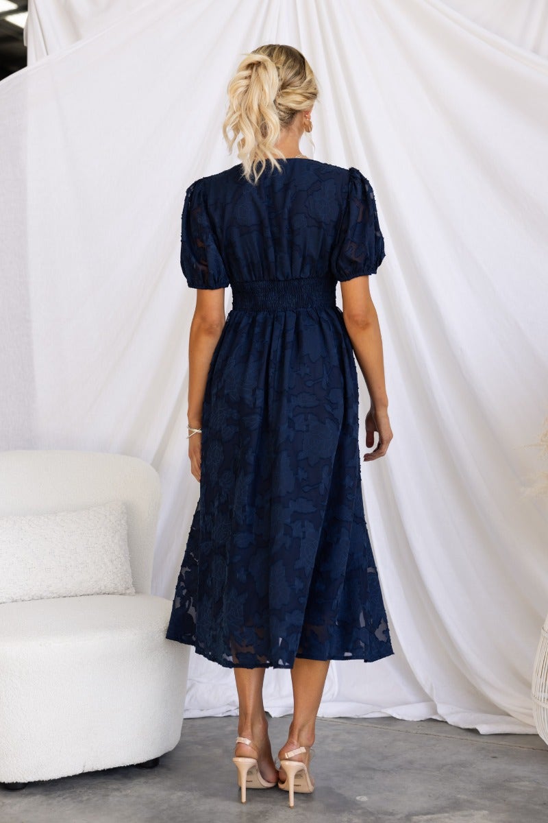 Back view of Narella Midi Dress in navy with embossed print and puff sleeves, showcasing its elegant fit and design.