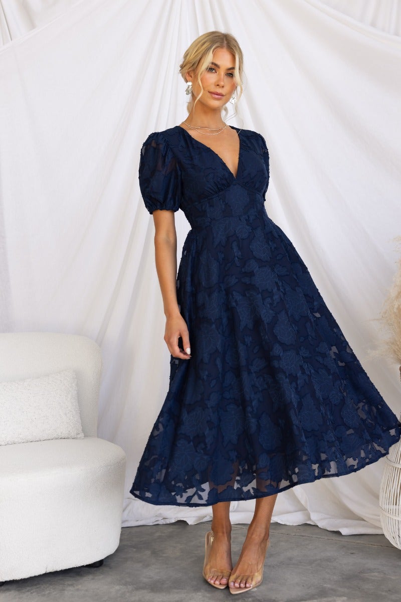 Narella Midi Dress in navy with embossed print, V-neckline, puff sleeves, and pockets, modeled by a woman.
