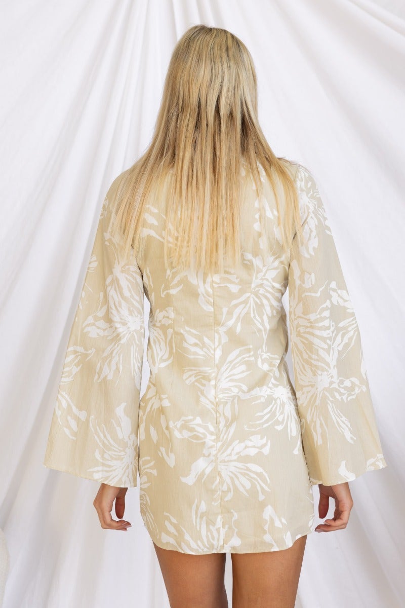 Back view of the Take Chances Dress, featuring a floral print and bell sleeves in a soft beige color.
