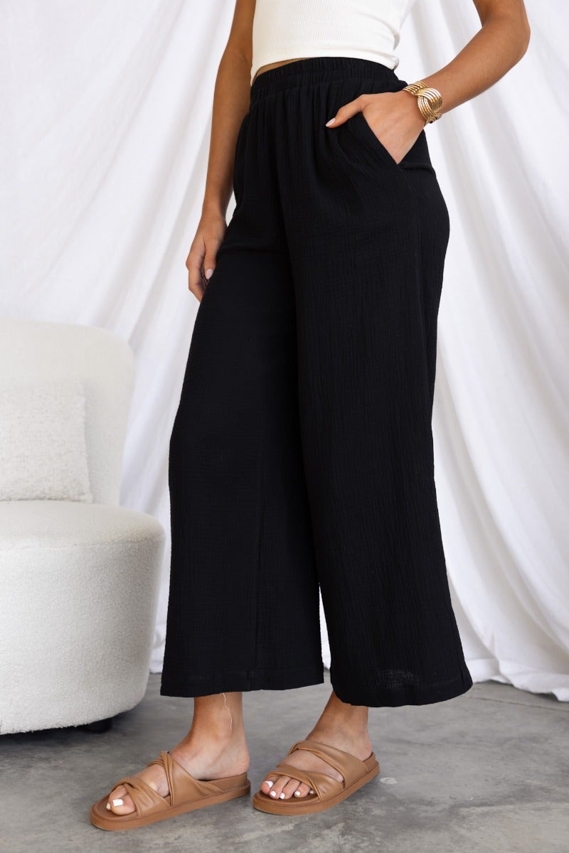 Eureka Pants: black cotton blend wide-leg pants with elastic waistband and pockets, modeled by a woman.