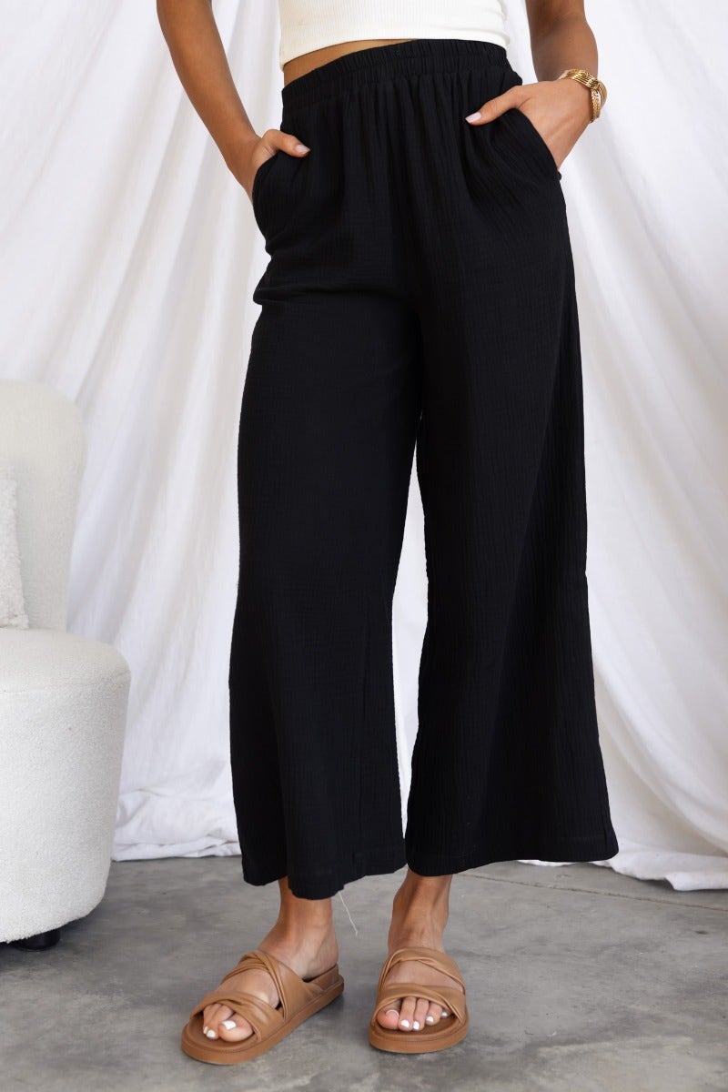 Eureka Pants: Black wide-leg cotton blend pants with elastic waistband and pockets, styled with casual sandals.