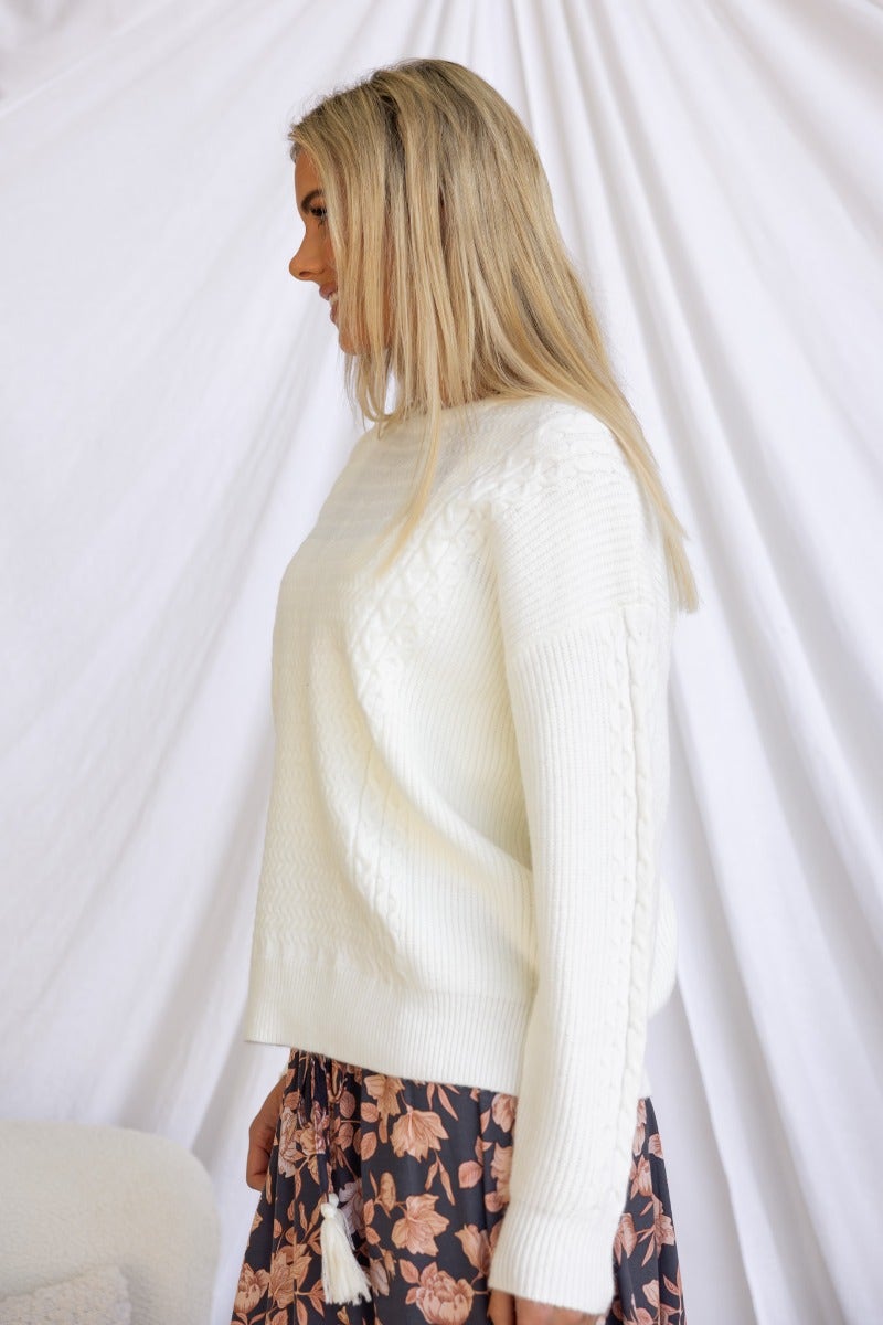 Side view of a model wearing a white knit jumper with round neckline, styled with a floral skirt.