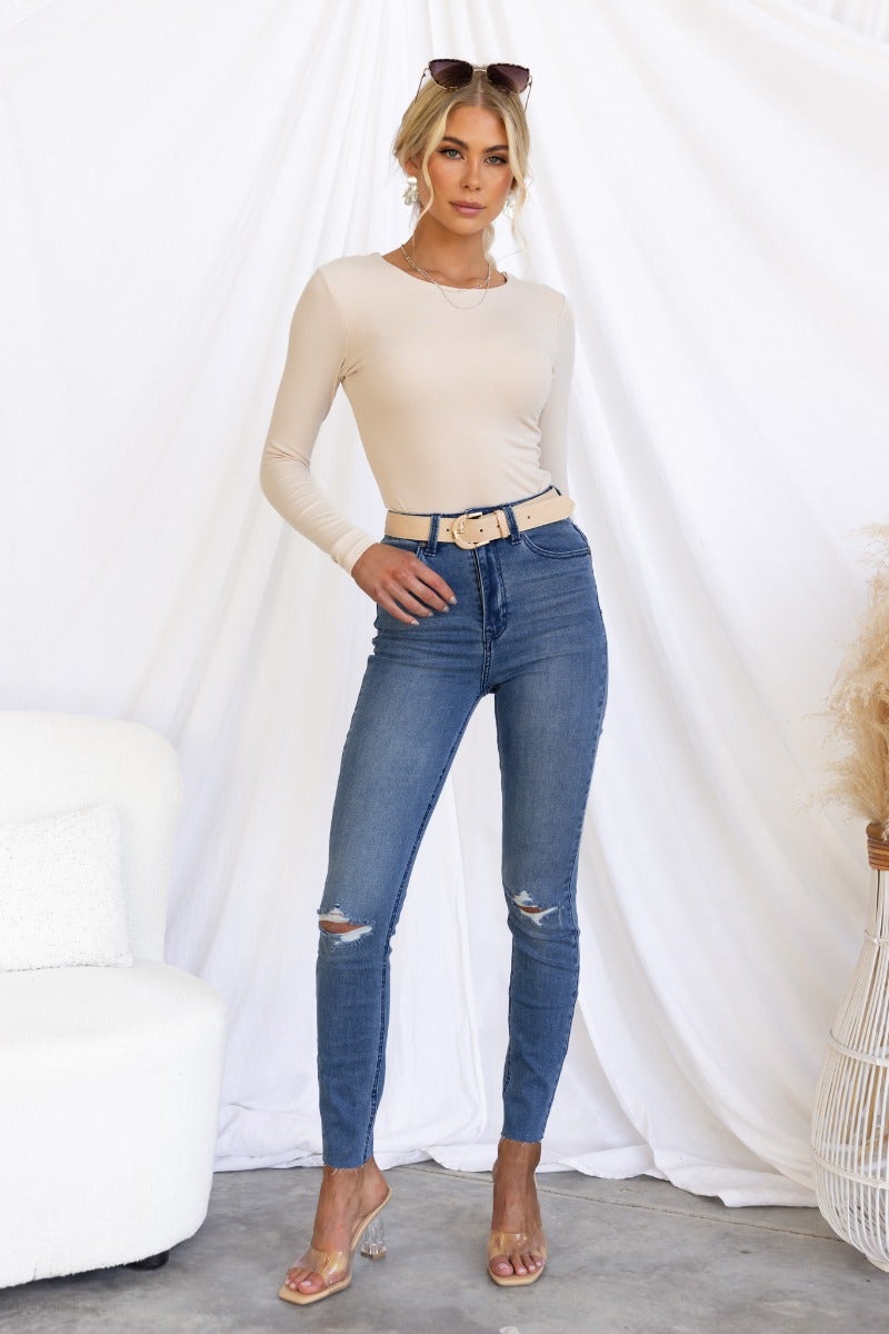 Model wearing Zira Top in beige with jeans, showcasing long sleeves and a round neckline.