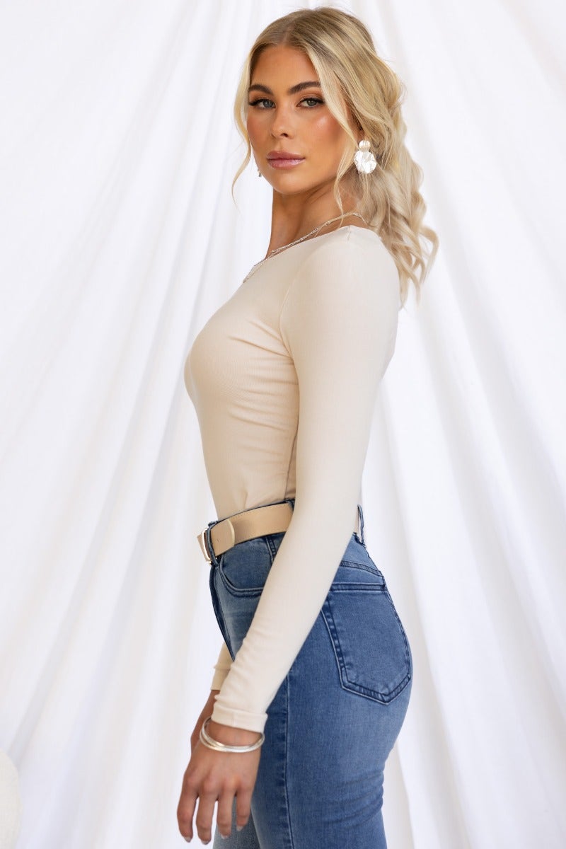 Model wearing Zira Top, a fitted beige long sleeve cotton top paired with high-waisted jeans.