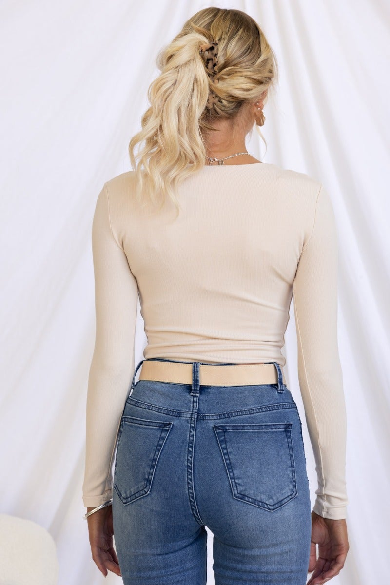 Back view of a model wearing a beige Zira Top with long sleeves paired with blue jeans.