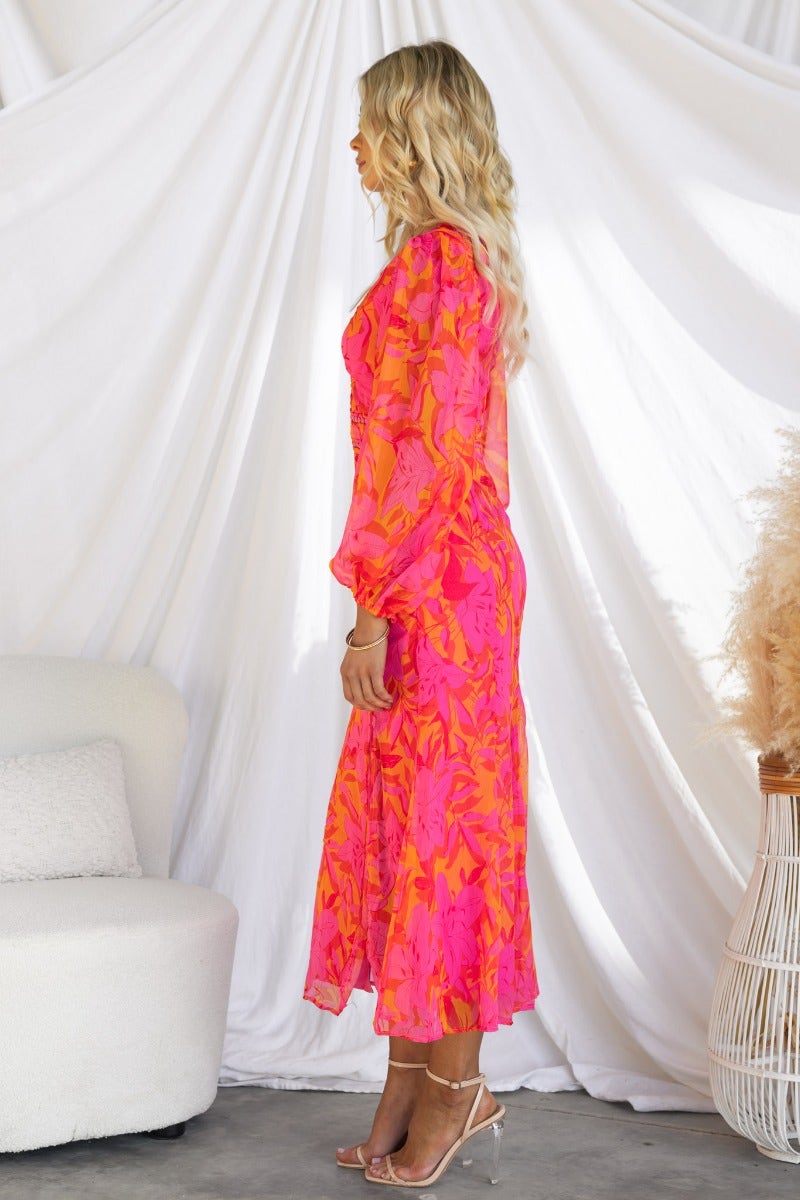 Side view of a model wearing a vibrant pink floral midi dress with elastic sleeve cuffs and a front split.