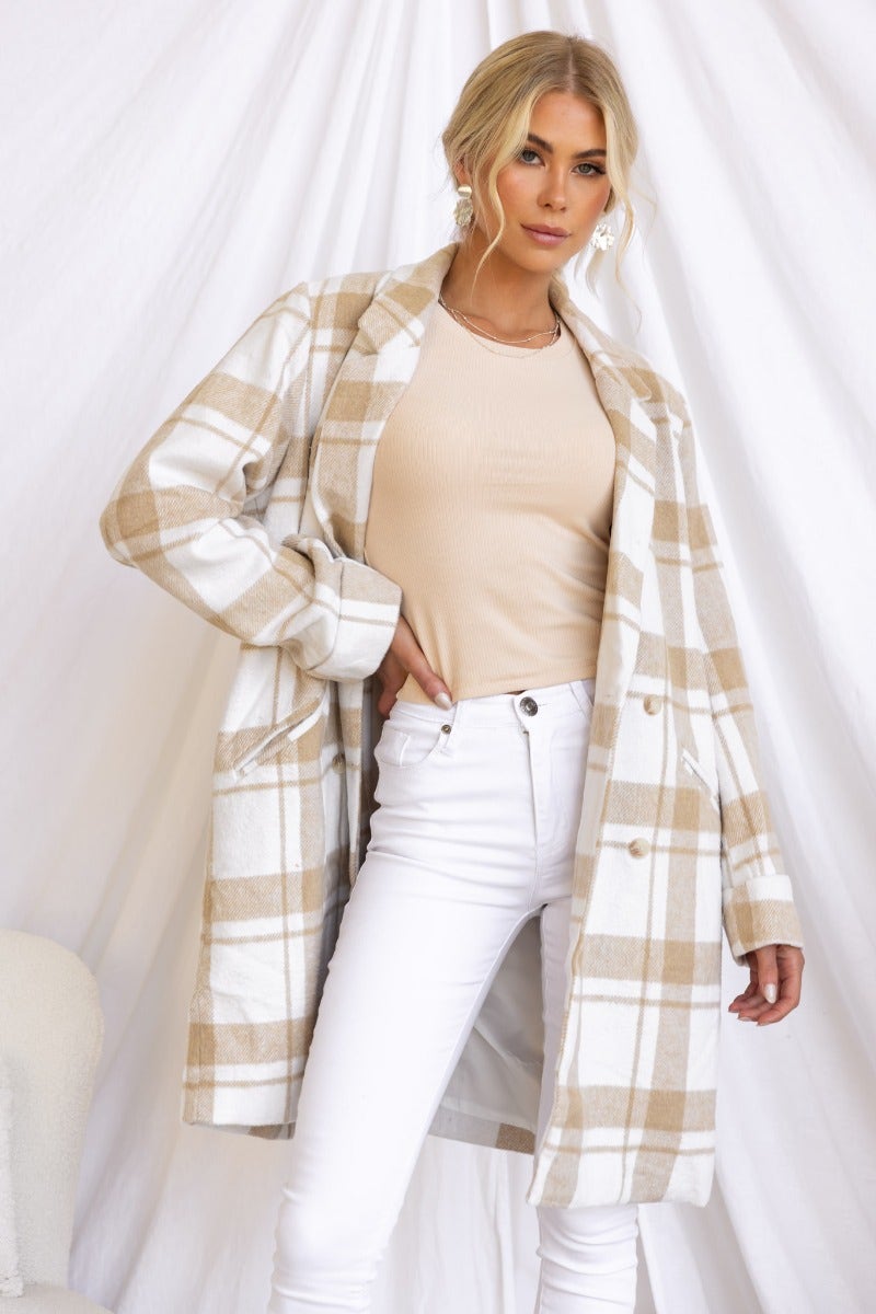 Model wearing the Sabine Coat, a plaid print coat with a button closure and faux pockets, styled with white jeans.