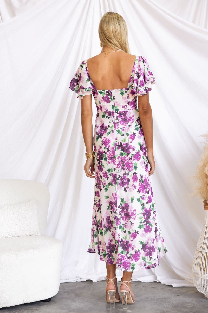 Back view of a Kamina floral print maxi dress with tie detail, showcasing ruffled sleeves against a white backdrop.