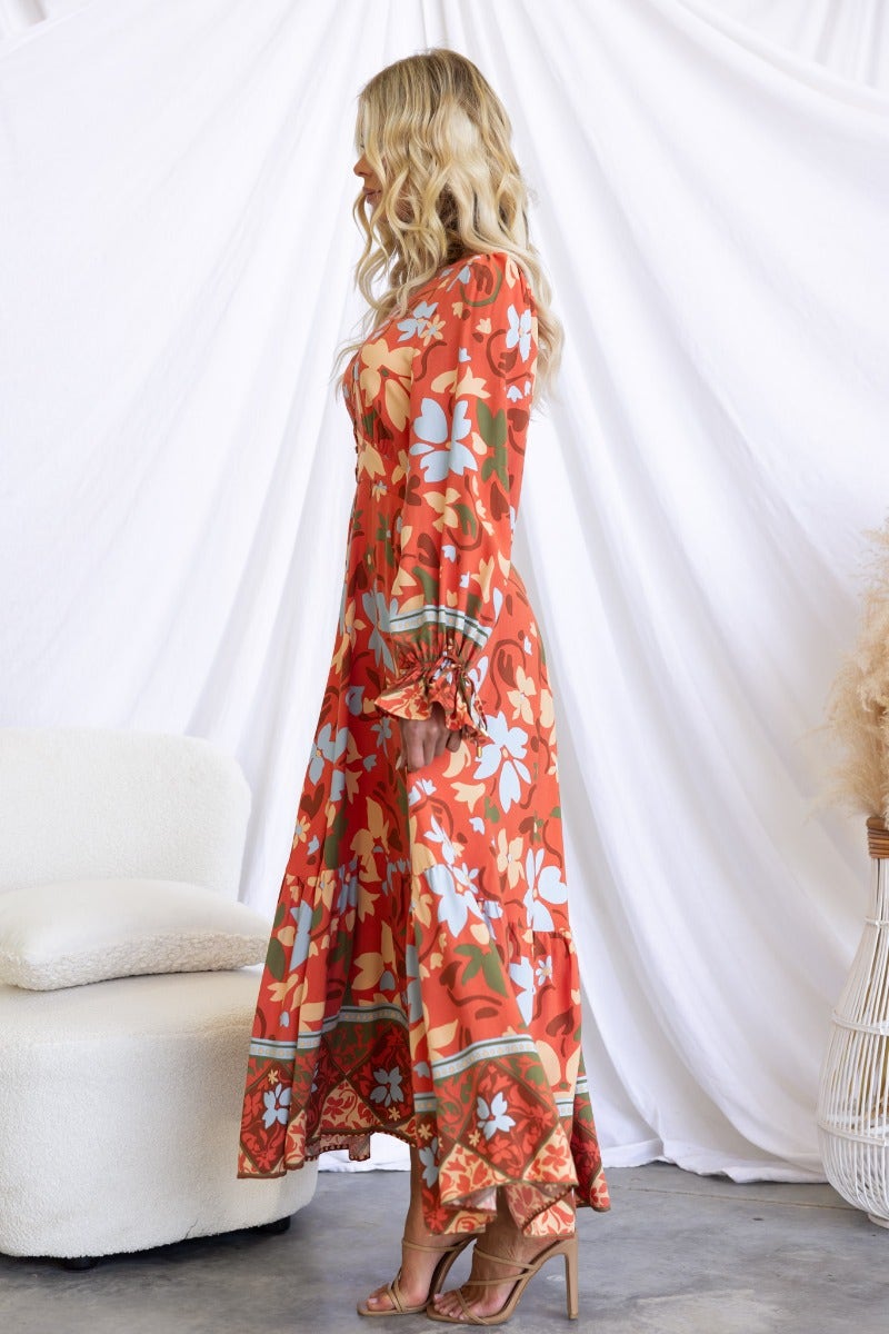 Side view of Taniah Maxi Dress in floral print, featuring V-neckline and elastic cuffs, styled with heels.