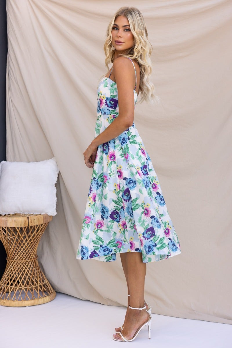 Rekiah Midi Dress with floral pattern, thin straps, and square neckline, modeled by a woman with wavy hair.