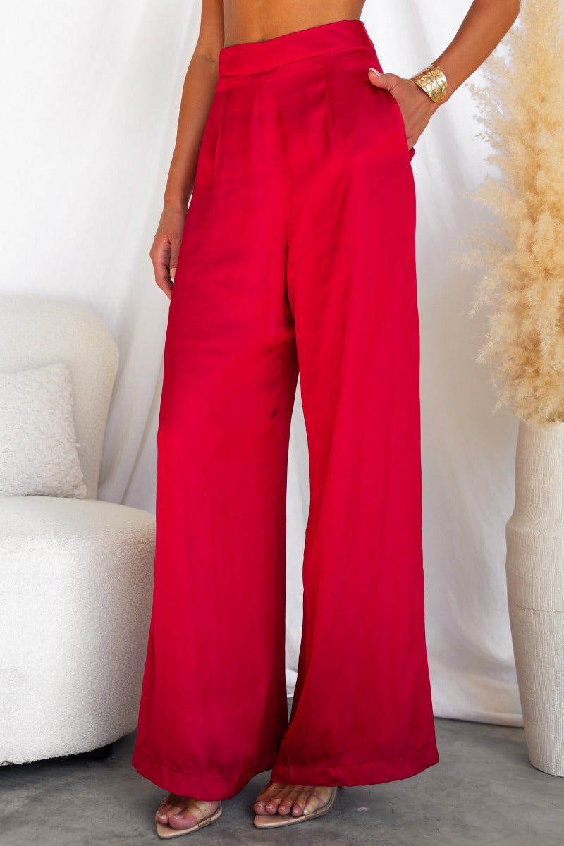 Red satin wide-leg pants with back zip and pockets, modeled by a woman, showcasing stylish casual wear.