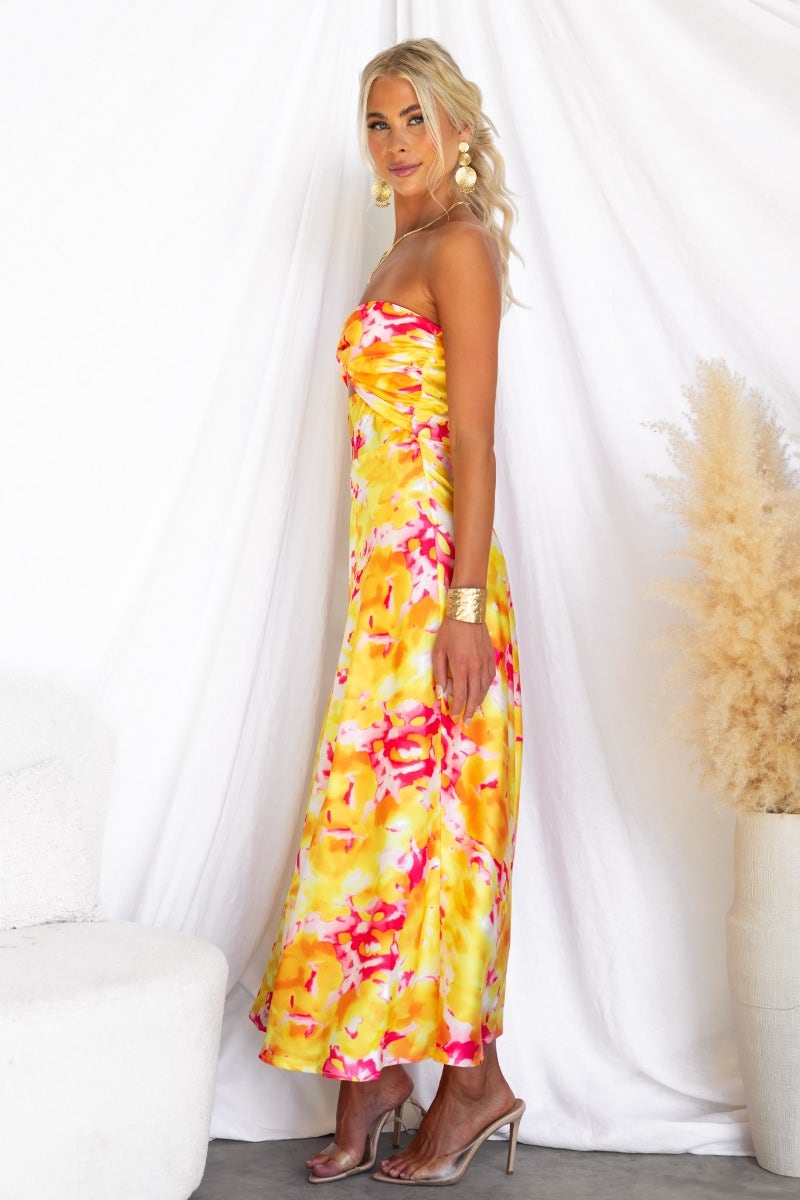 Model wearing a vibrant Electric Touch Maxi Dress with a strapless design and floral pattern, standing against a textured backdrop.