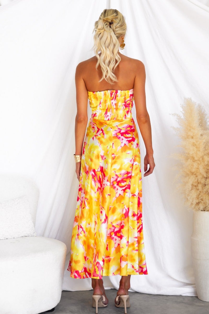 Back view of a woman in a vibrant pink and yellow satin strapless maxi dress, featuring an elastic back and cut-out detail.