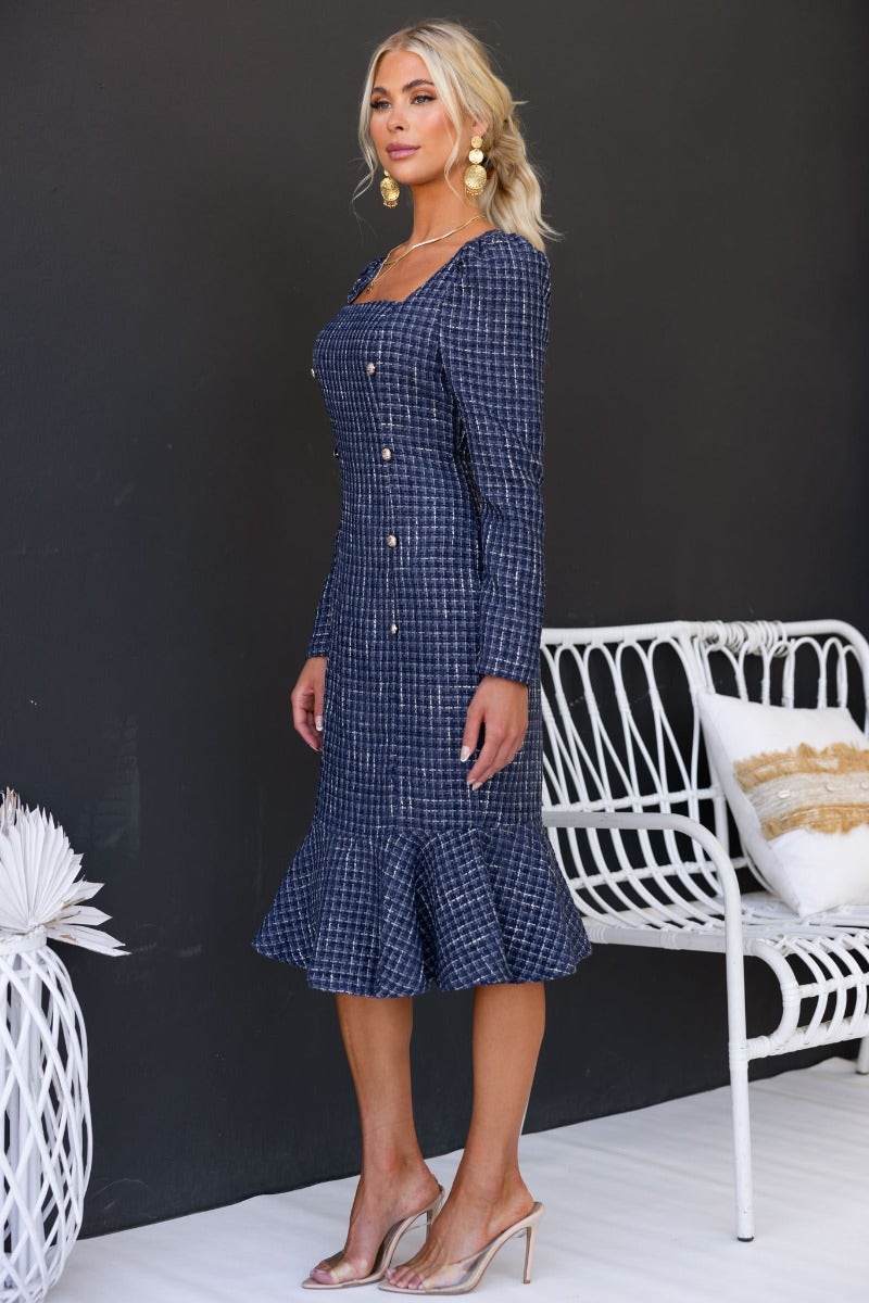 Model wearing a blue tweed midi dress with a square neckline and gold button details, styled with clear heels.