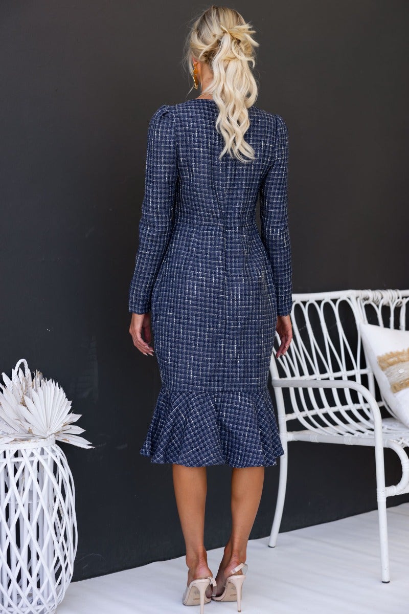 Back view of a woman in a fine line midi dress with a fitted silhouette and flared hem.