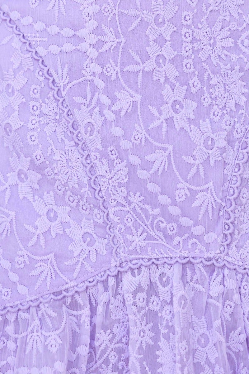 Close-up of embroidered lavender fabric showcasing intricate floral patterns and detailed stitching.