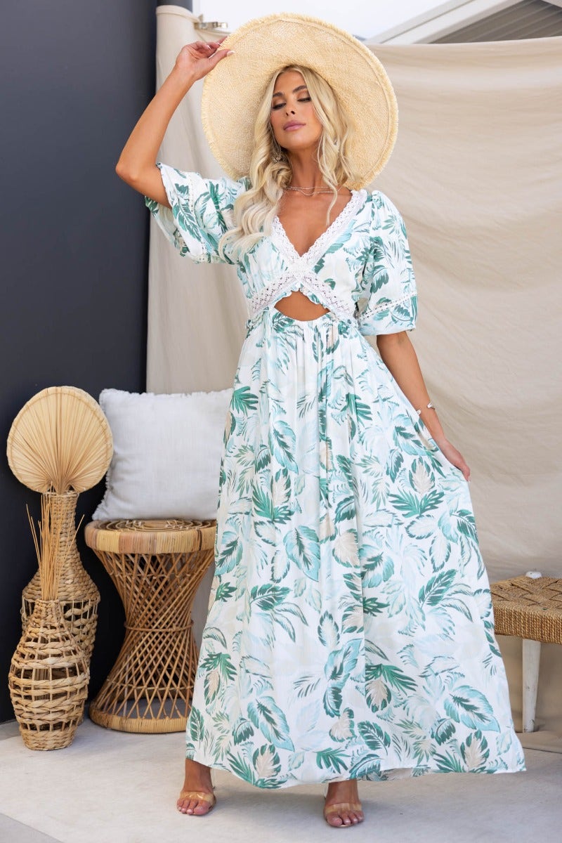Model wearing Out Of Sight Maxi Dress with floral print, v-neckline, and cut-out waist, complemented by a straw hat.
