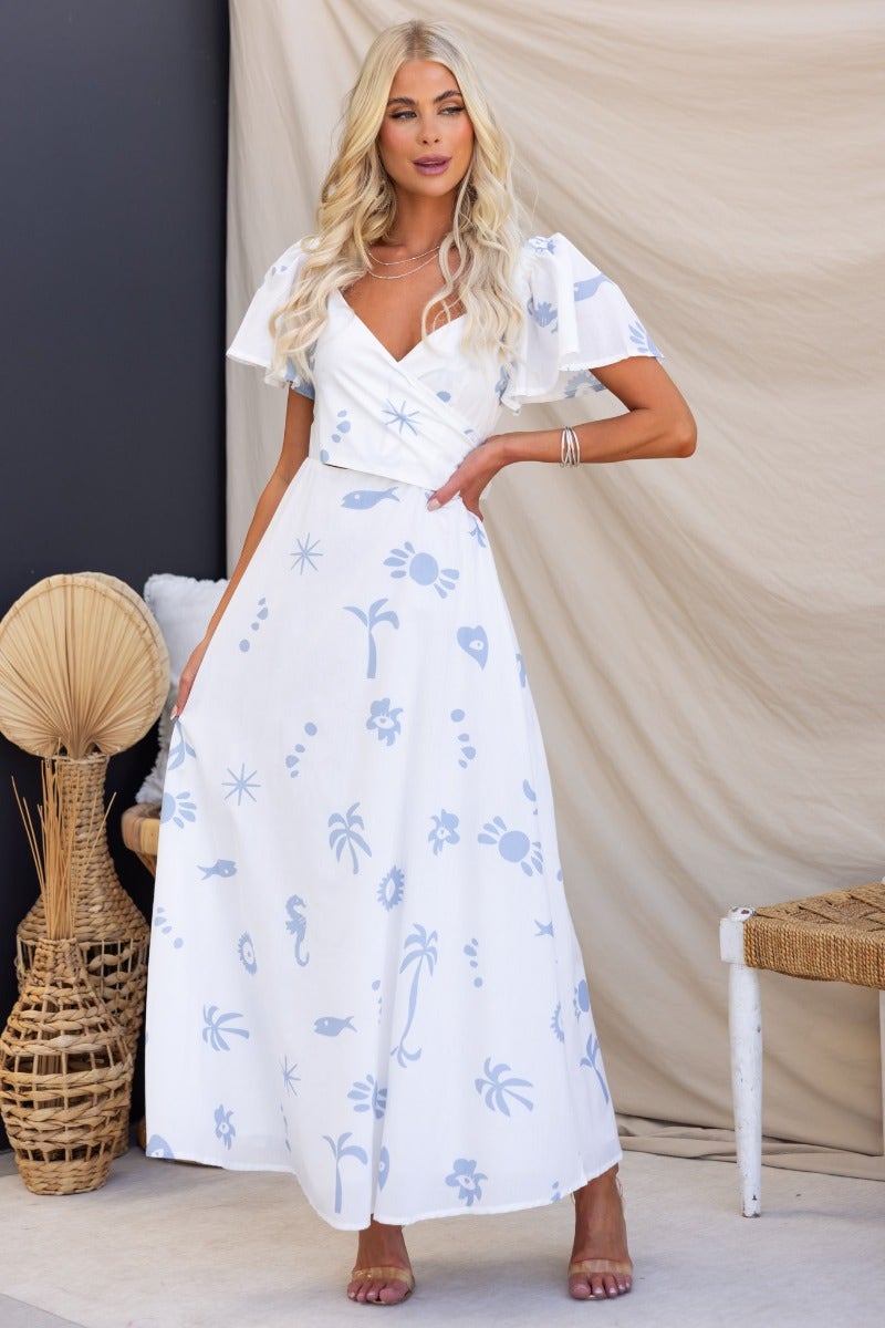 Fermina Wrap Maxi Dress in white with blue floral print, featuring elastic sleeve fittings and a wrap tie at the bust.