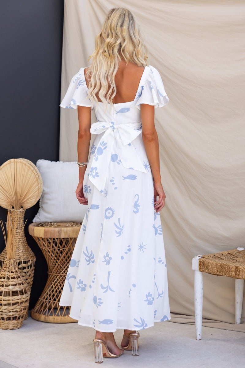 Back view of a feminine white wrap maxi dress with floral patterns and a bow detail, perfect for summer events.