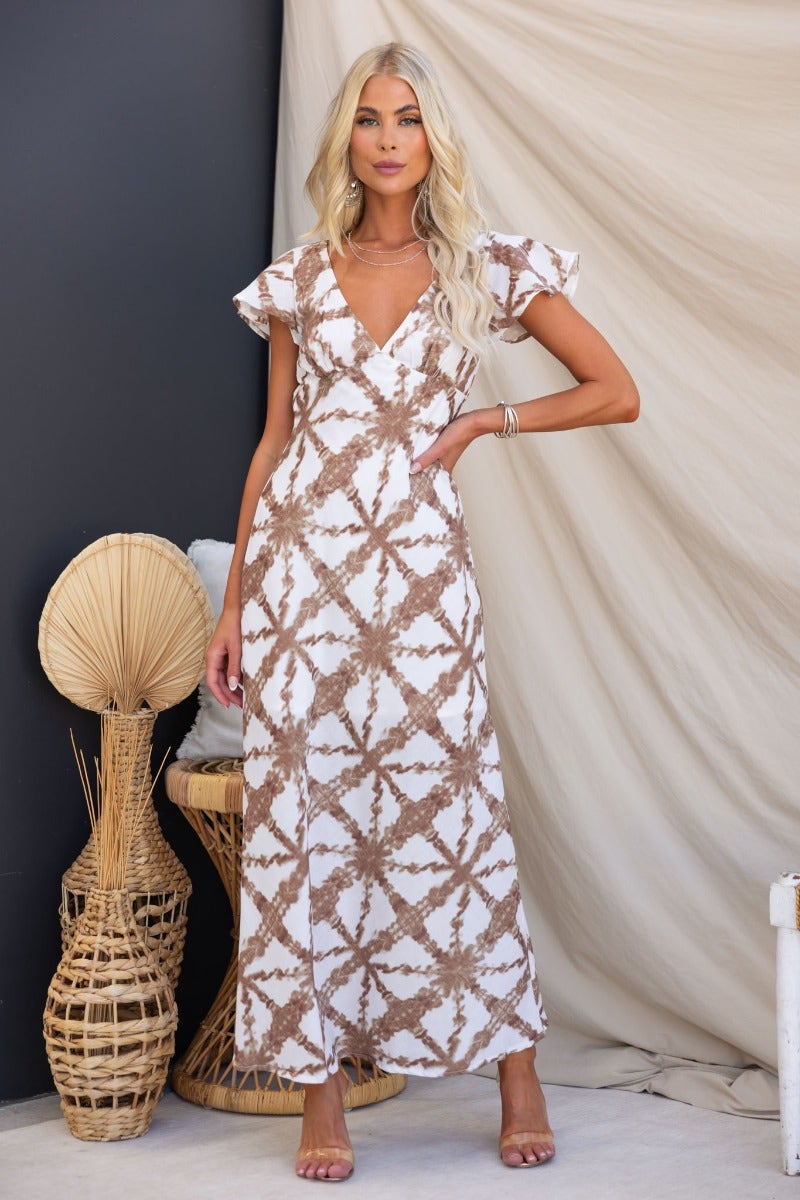 Elegant Cynthia maxi dress with V-neckline, tie detail, and patterned fabric, styled in a chic setting.