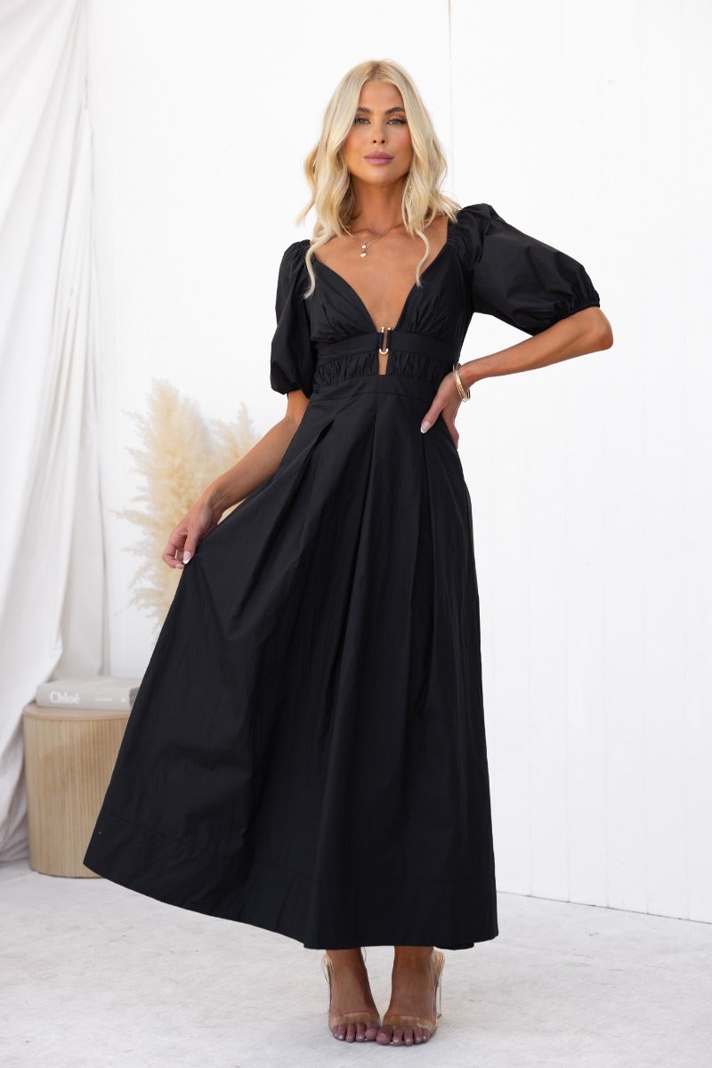 Model wearing The Climb Maxi Dress, a black cotton dress with V-neckline and puff sleeves, showcasing elegant style.