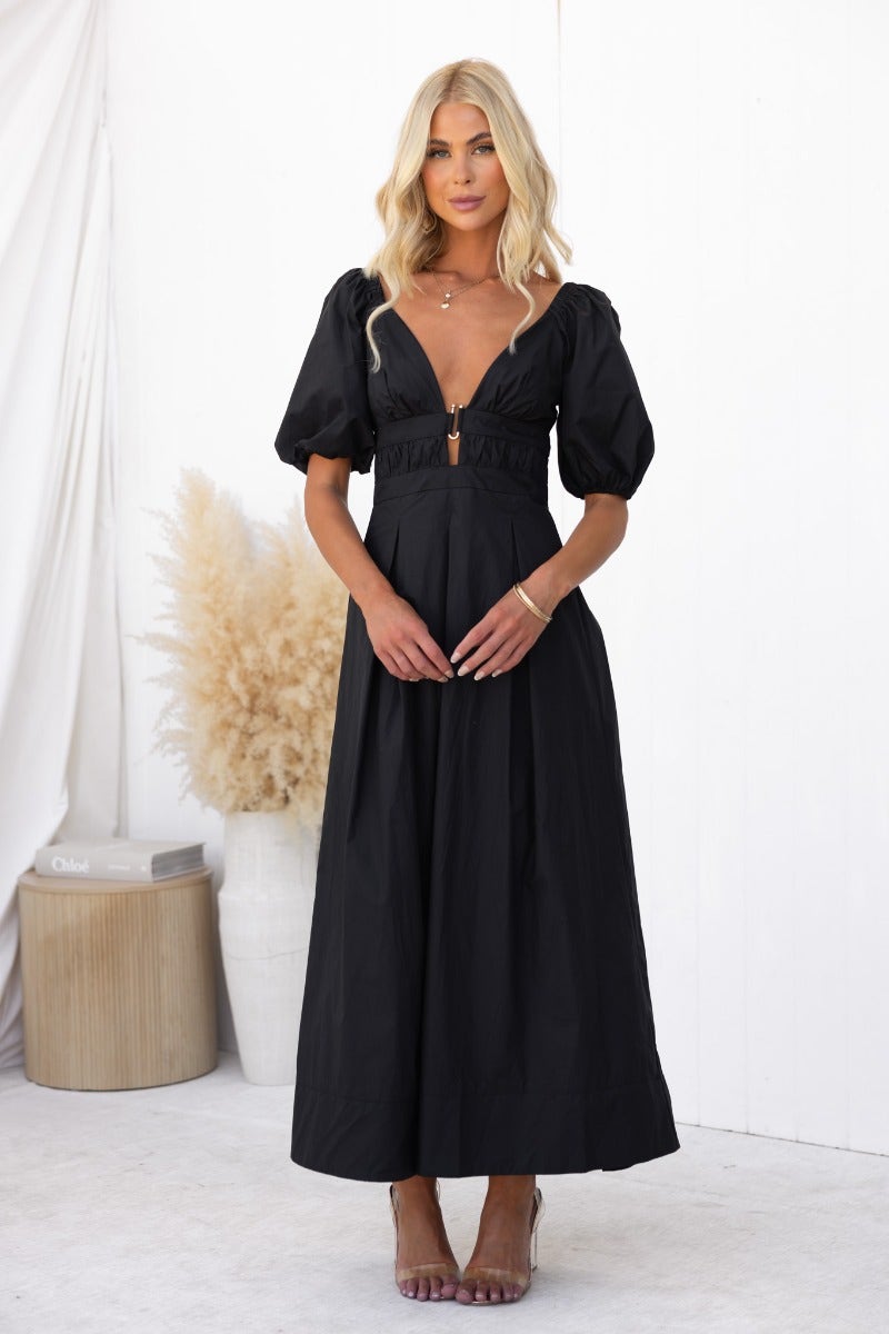 A model wearing a black cotton maxi dress with a V-neckline and puff sleeves, featuring gold hardware and an invisible zip.