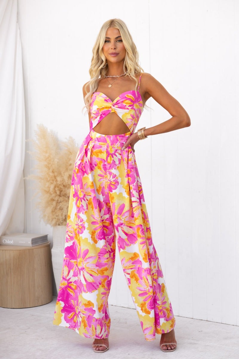 Floral print Ivy jumpsuit with adjustable straps and cut-out detail, styled by model in pink and yellow hues.