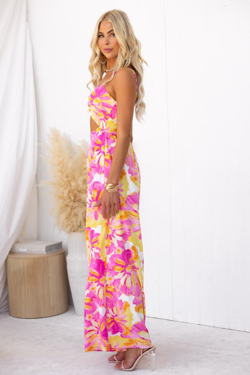 Side view of a model wearing a floral print Ivy jumpsuit with adjustable straps and a twist detail.