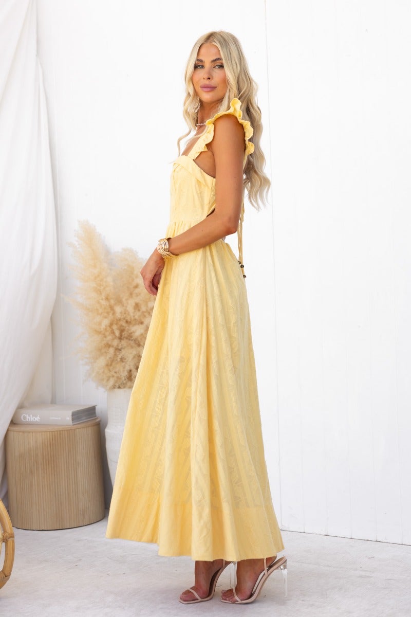 Model wearing a yellow Fiji Maxi Dress with ruffled straps and a flowing design, set against a bright background.