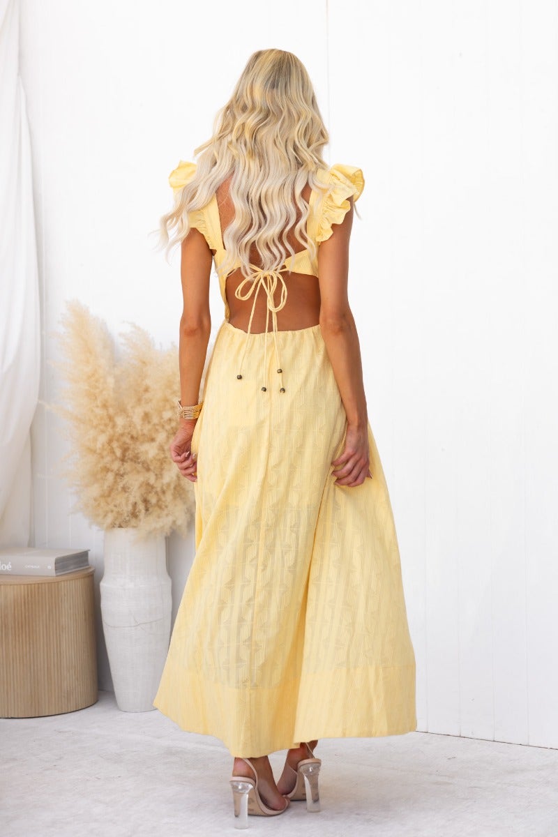 Back view of a model wearing a yellow Fiji Maxi Dress with ruffled sleeves and tie detail.