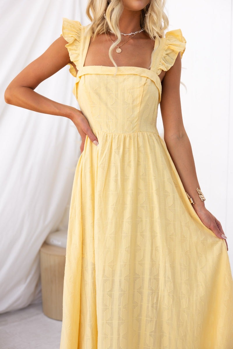Fiji Maxi Dress in textured yellow fabric with ruffle sleeves, showcasing a tie-back design and semi-sheer lining.