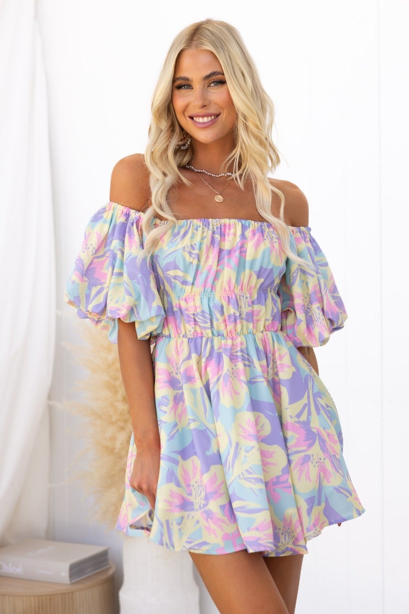 Model wearing Claire Dress, a mini off-shoulder dress with gathered fabric and floral print.