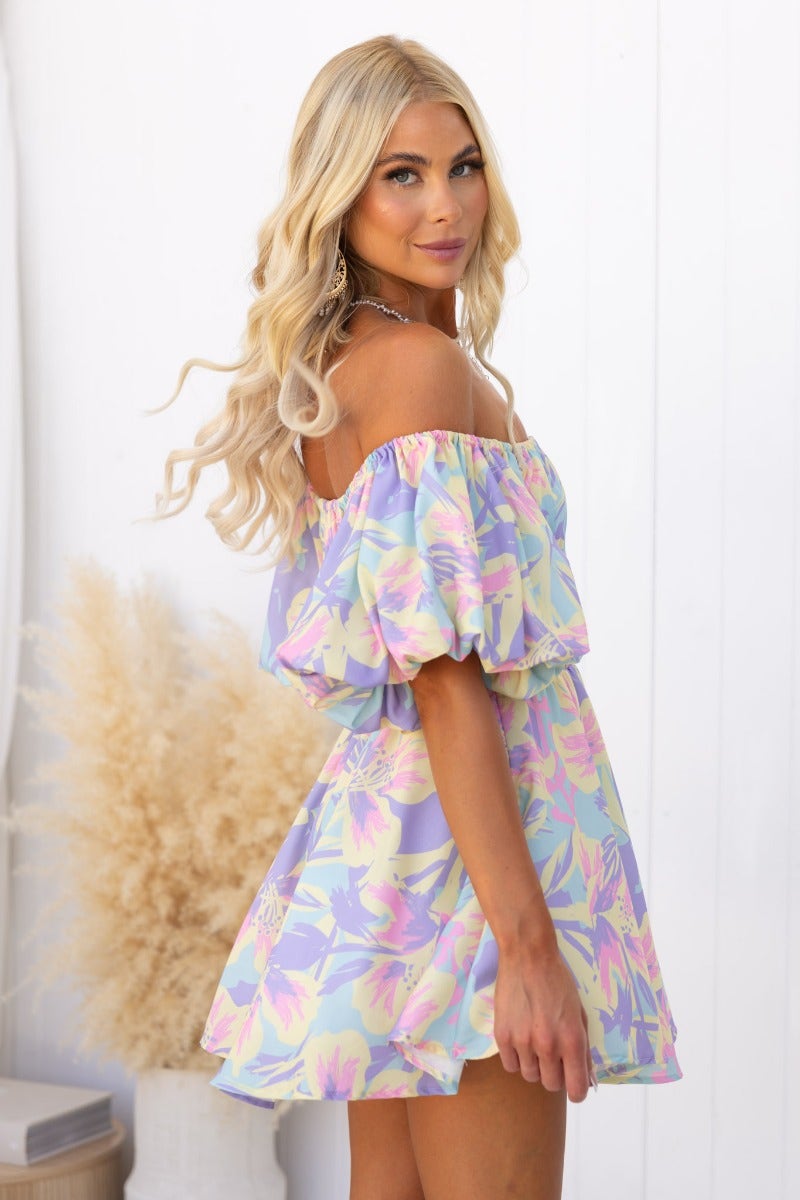 Model wearing the Claire Dress, featuring floral print, off-shoulder neckline, and gathered bodice details.