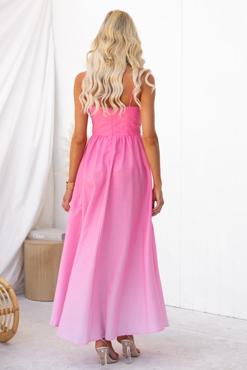 Back view of a woman wearing a pink cotton blend maxi dress with adjustable straps and a flowing silhouette.