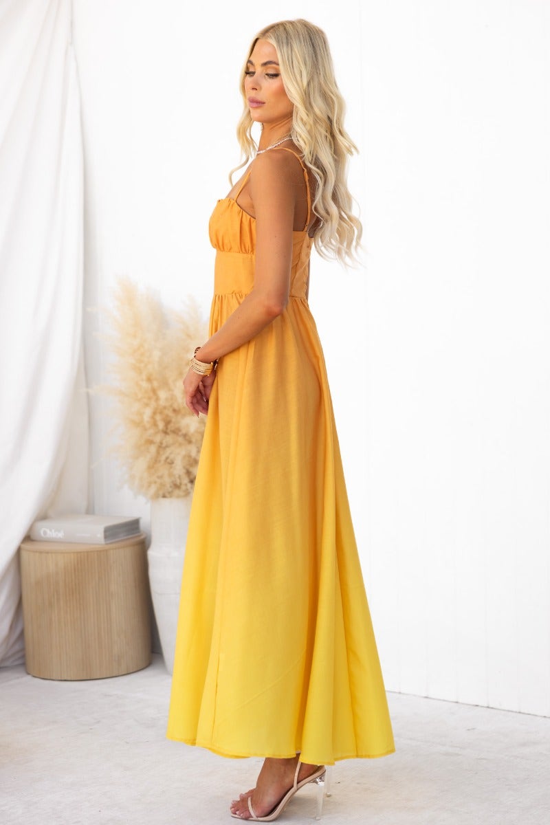 Woman wearing a cotton blend Blank Space Maxi Dress in vibrant yellow, featuring adjustable straps and a flowing silhouette.