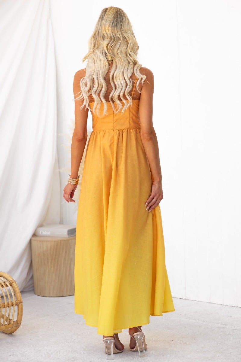 Back view of a woman in a yellow cotton blend maxi dress with adjustable straps and a flowing skirt.
