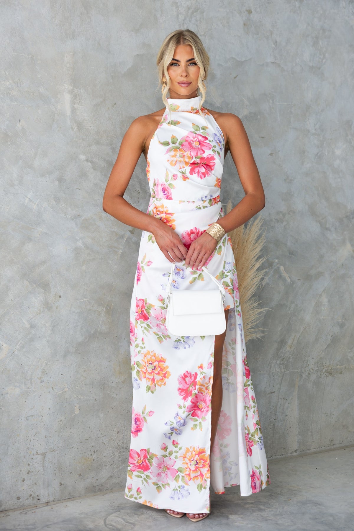 Floral print Levona maxi dress with high neckline, asymmetric hemline, and elegant satin finish, styled with a white handbag.