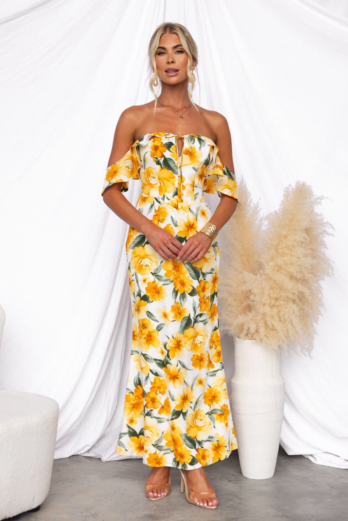 Floral print off-shoulder maxi dress with tie detail and side zip, styled with a minimalist backdrop.