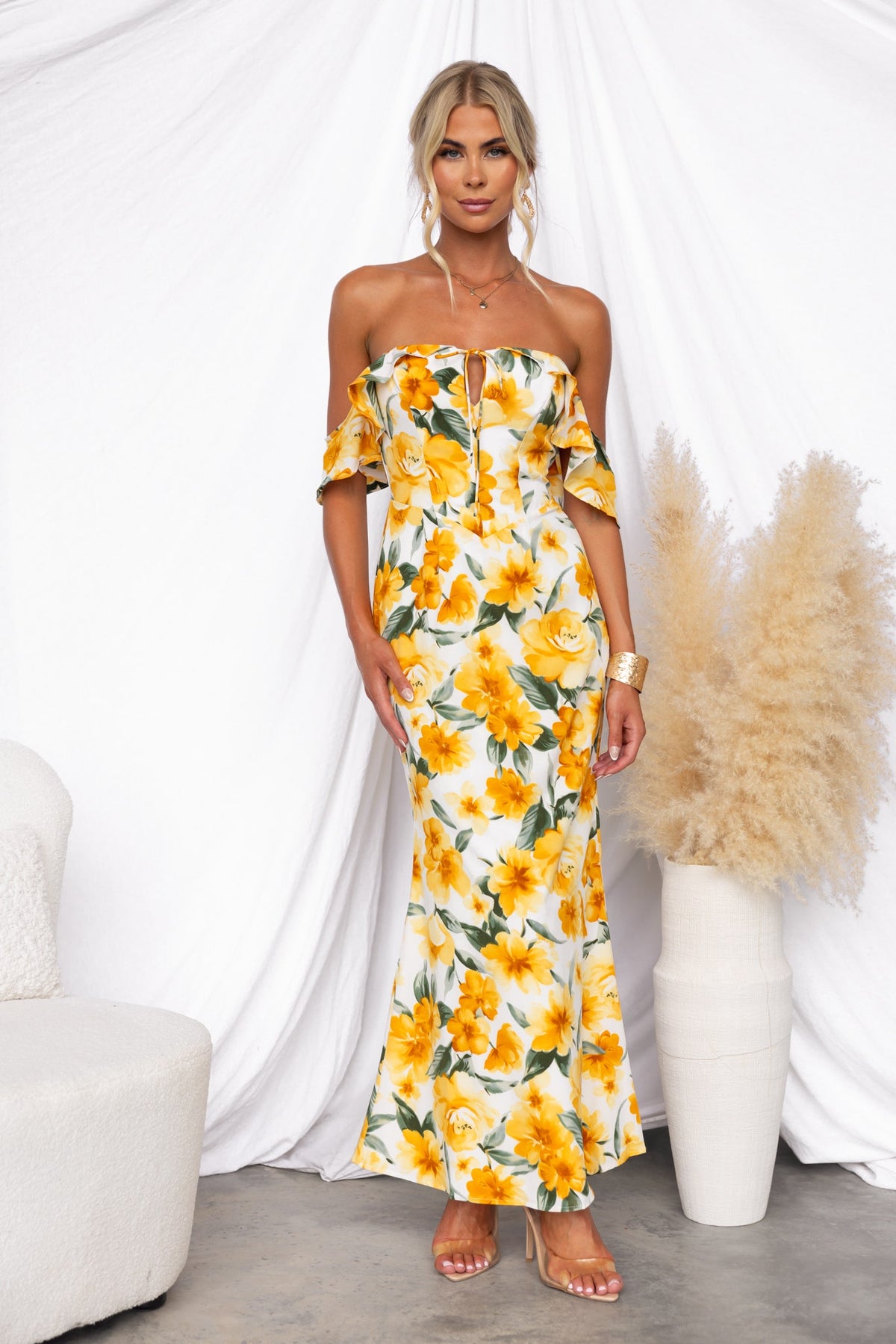 Floral print off-shoulder maxi dress with a tie detail and side zip, styled on a model against a textured backdrop.