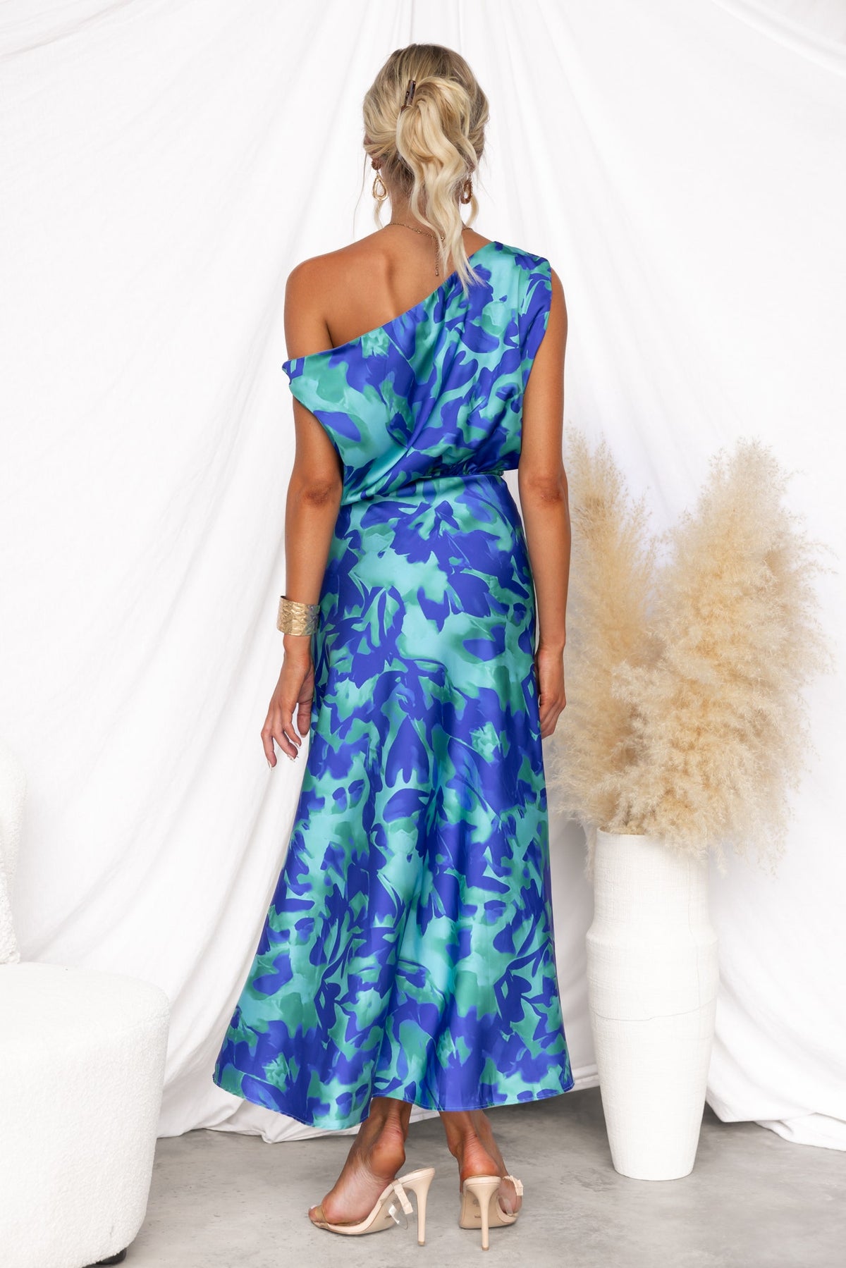 Sicilian Sun Maxi Dress featuring floral print, asymmetric neckline, and satin finish, styled with chic accessories.