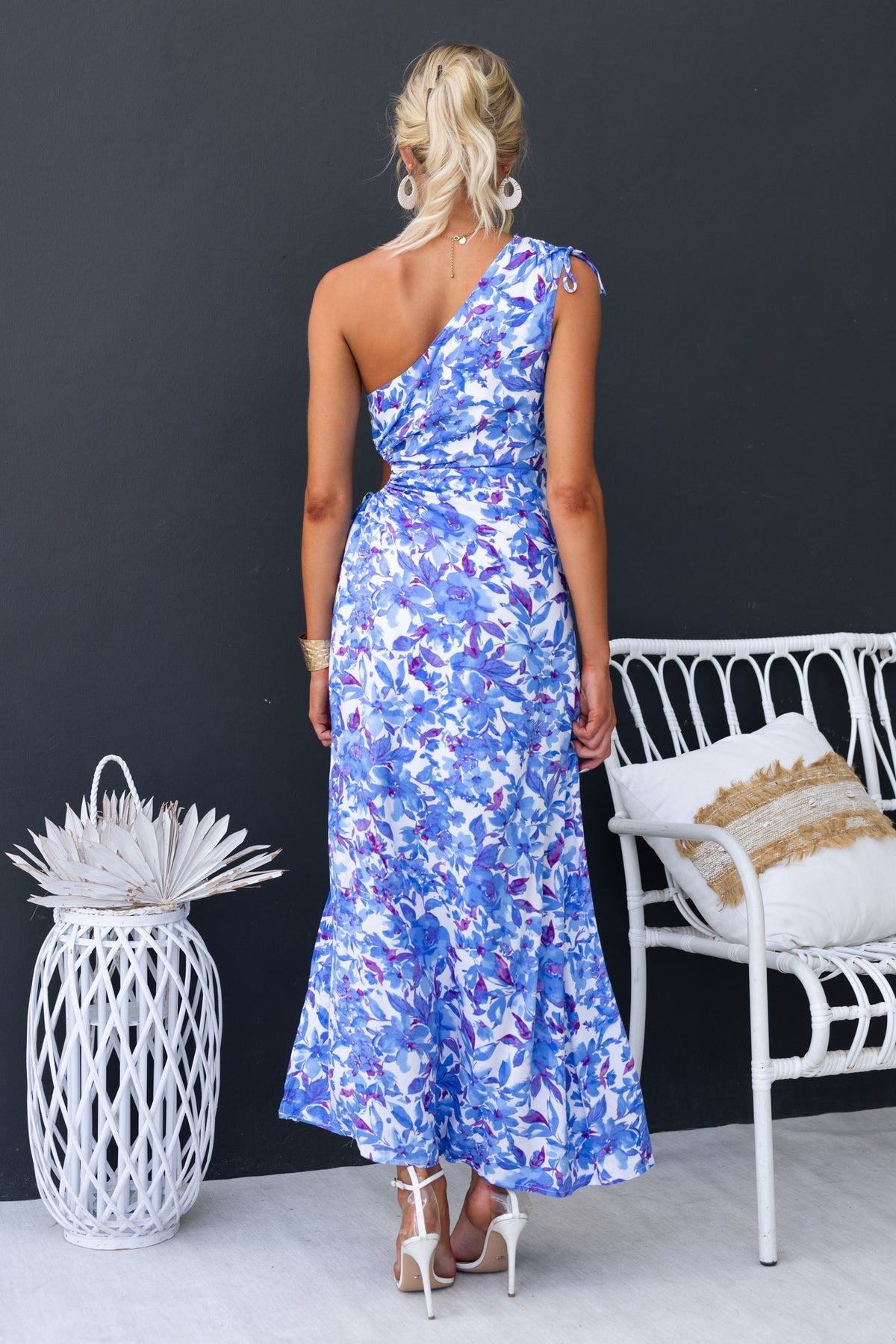 Back view of a woman in a floral print one-shoulder maxi dress, showcasing adjustable ruching and a split skirt.