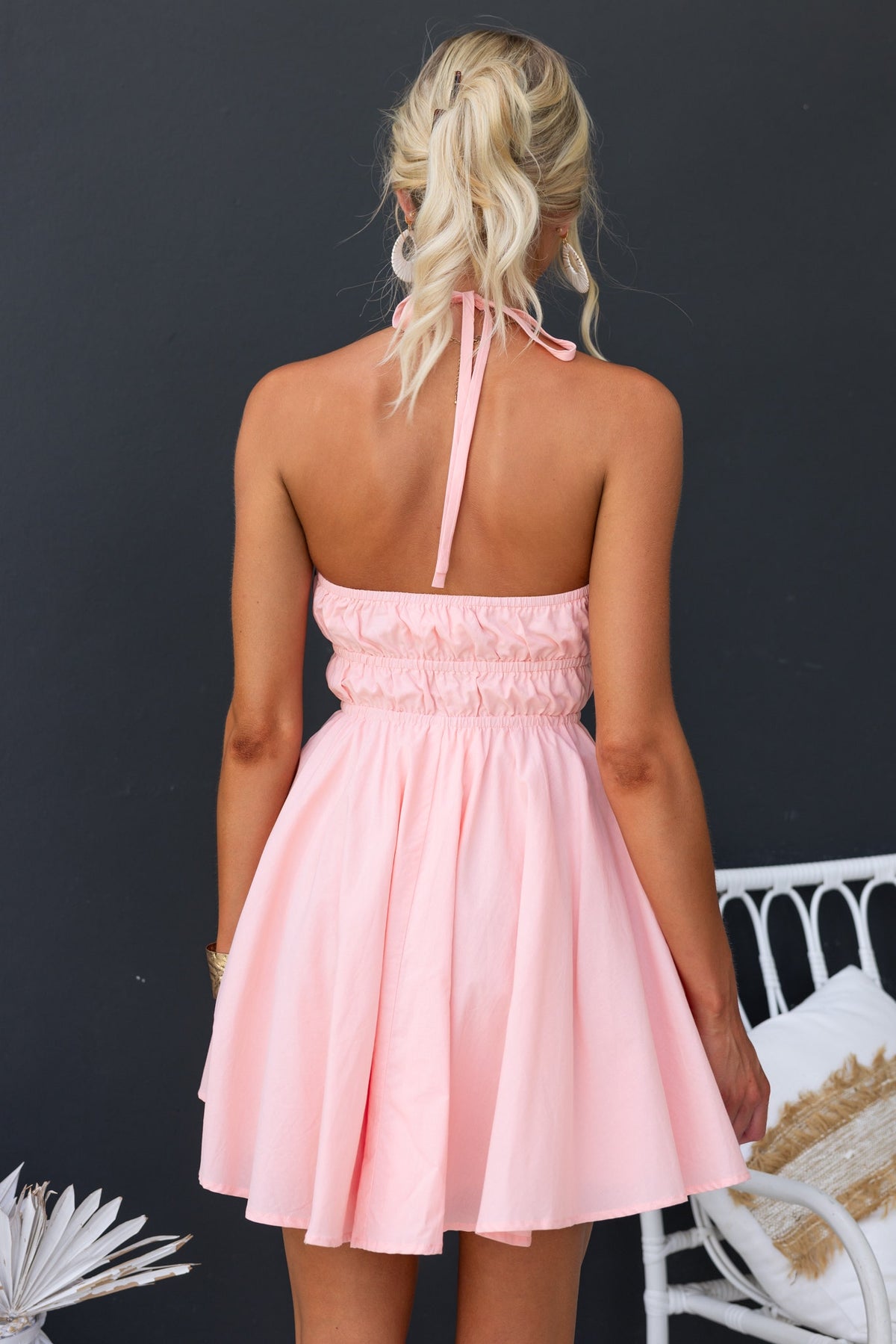 Back view of a model wearing a pink mini dress with an adjustable tie neckline and elastic detailing.