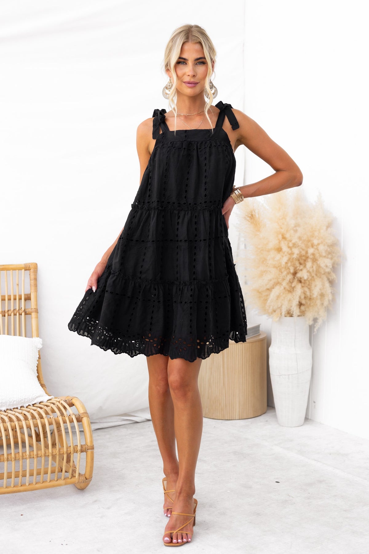 Model wearing a black Charlene Dress with adjustable tie straps, featuring a tiered design and Anglaise material.