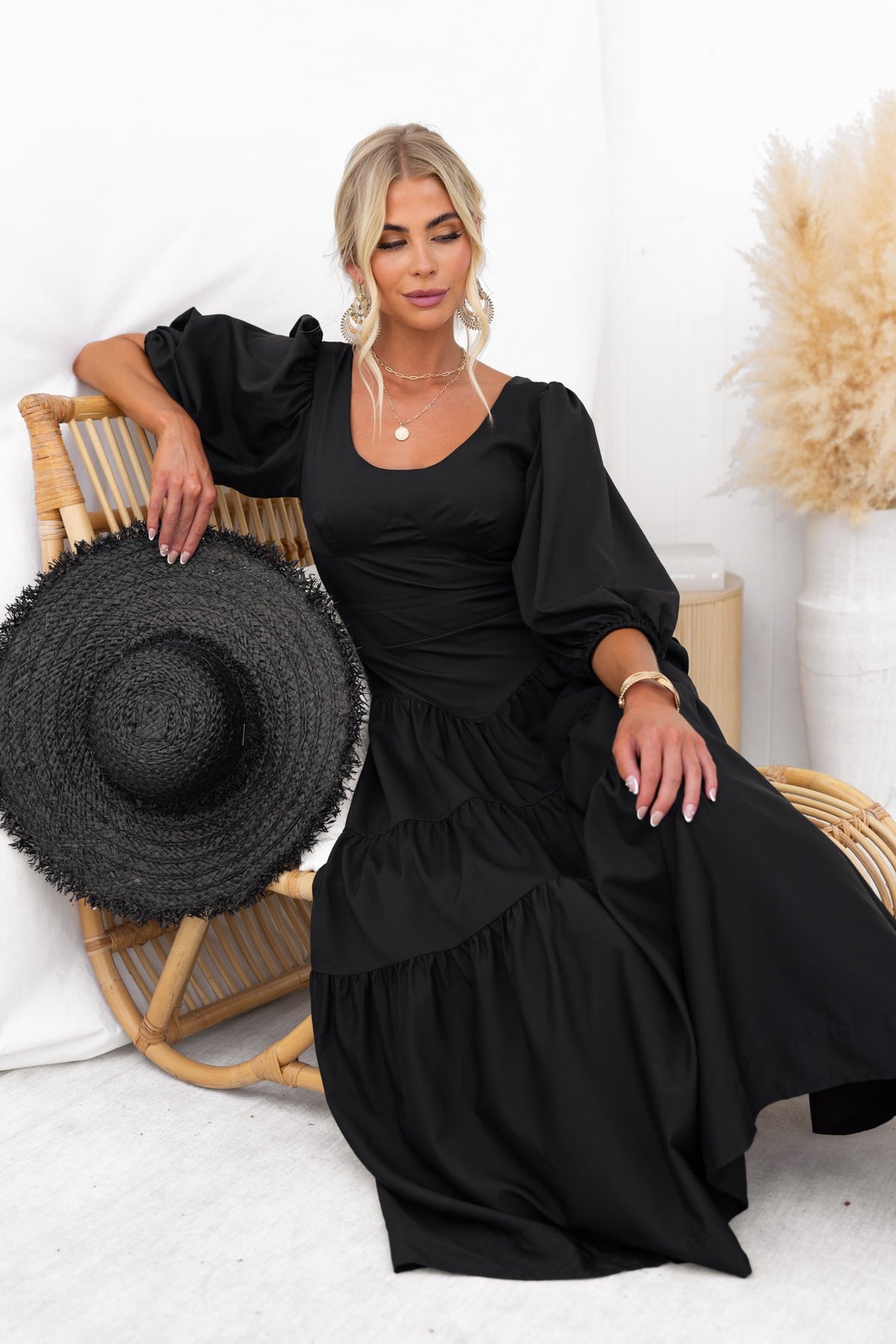 Model wearing a black Merle Midi Dress with round neckline and puff sleeves, styled with a straw hat.