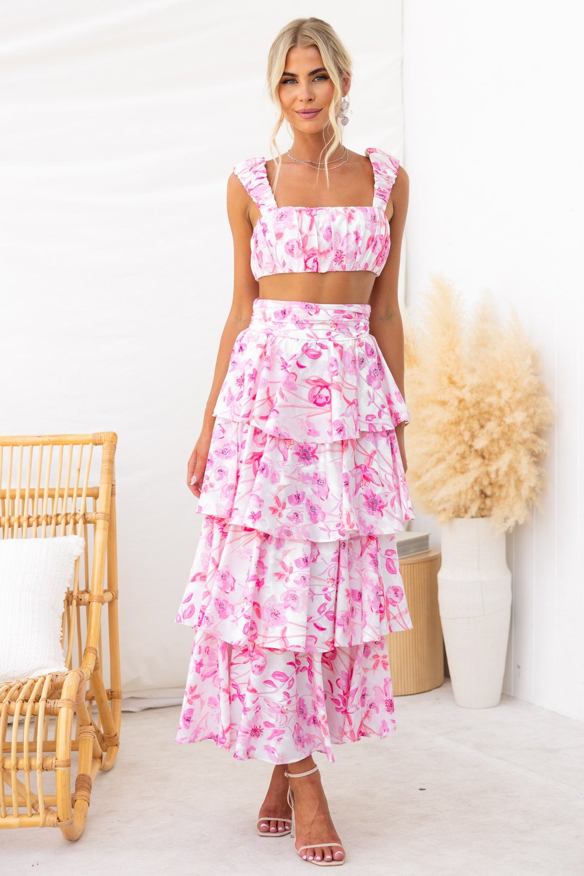Floral print illusion set featuring gathered top and ruffle maxi skirt in pink, styled with a relaxed background.