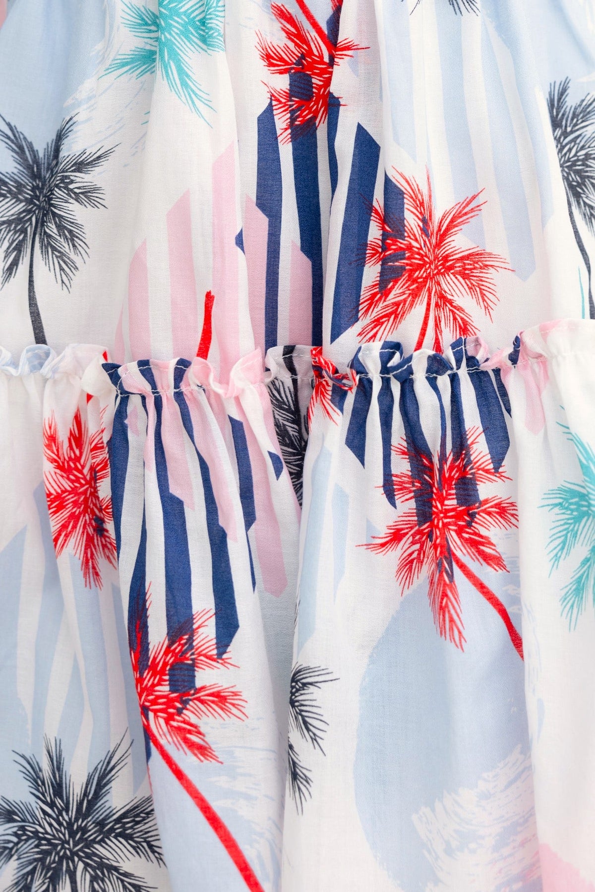 Close-up of Lorie Dress featuring floral print with palm trees and stripes, showcasing adjustable tie neckline and gathered waist.