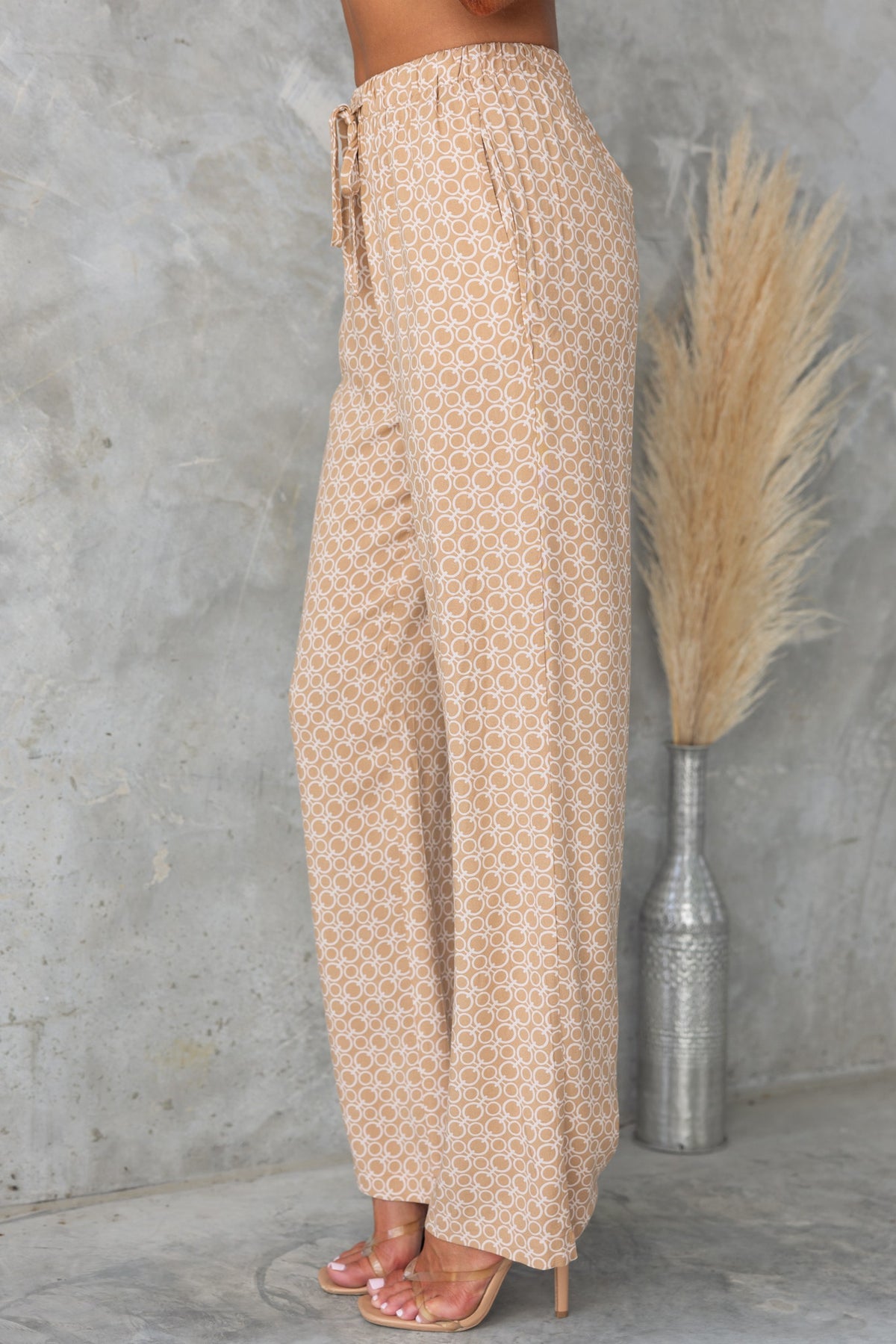 Side view of Okar Pants with abstract print, mid-high waist, elastic waistband, and pockets, styled with heeled sandals.